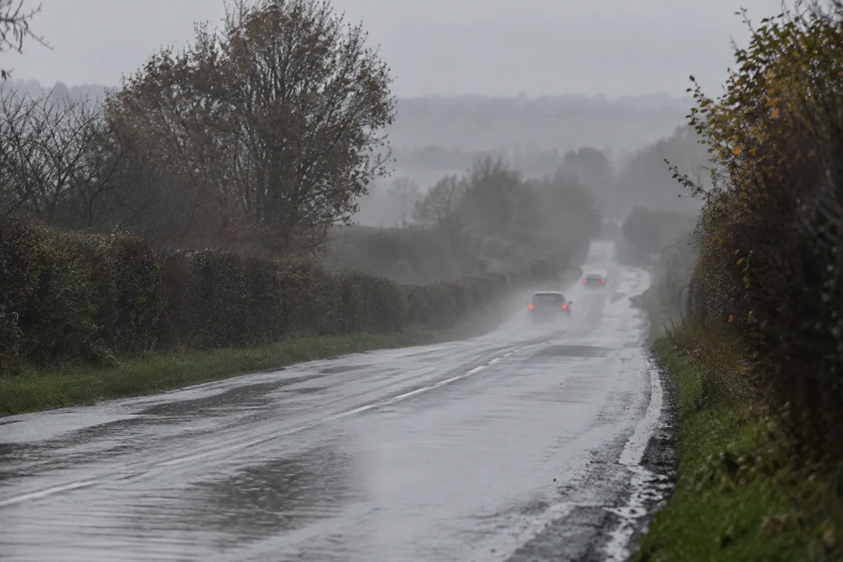 Voiture vue de l&rsquo;arrière roulant à bonne distance d&rsquo;une autre sur une route départementale mouillée sous une pluie fine