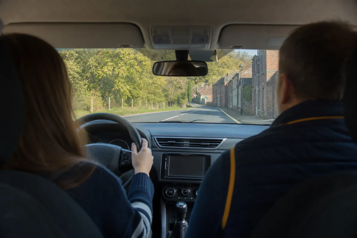Élève et enseignant de la conduite dans l’habitacle d’une voiture école, mains sur le volant